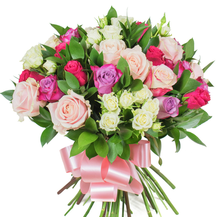 Set against a brilliant white studio backdrop, this dense, rounded bouquet presents an artful blend of classic and modern rose varieties in a harmonious celebration of pinks, purples, and creams. Broad, fully opened roses in soft pastel pink and creamy white anchor the arrangement, their gently ruffled petals revealing delicate veining and a satiny texture; brighter, hot-pink and magenta roses appear as bold accents that animate the composition, while a scattering of light lavender roses introduces a subtle, romantic coolness. Interlaced throughout are clusters of small spray roses in pristine white with pale-yellow hints, adding fine detail and a varied scale that deepens the visual field. The abundant deep-green foliage - glossy, elongated leaves suggestive of ruscus or salal - is carefully placed to create pockets of shade and highlight each blossom's colour. The long stems are tightly gathered and wrapped with a wide, lustrous baby-pink satin ribbon, expertly tied into a flowing bow whose trailing tails soften the bouquet's base; the ribbon's sheen picks up the studio's soft lighting and complements the petals' muted radiance. The overall impression is of a bouquet that radiates celebration and affection, its textures and hues evocative of a gentle coastal breeze on the Isle of Dogs. Thoughtful and refined, it would make a touching gift for anniversaries, birthdays, or as a token of appreciation delivered locally to streets like East Ferry Road or the quieter lanes near Cubitt Town Green.