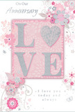 In this image, an anniversary card lies ready to accompany a bouquet, its design echoing the soft romance often requested for celebrations in Cubitt Town. The focal point is the word LOVE, written in large, uppercase letters that rise just enough from the card to create a gentle shadow. Each letter is edged with a fine dusting of glitter, producing a subtle silver sparkle that adds both glamour and texture. The inner surfaces of the letters are a creamy, pearlescent white, standing out beautifully against the warm blush-pink background. That pink tone is even and soothing, similar to the soft hues often used in anniversary arrangements for riverside homes, with a suggestion of deeper shading toward the card's edges that draws the eye inward. Encircling this central word, an intricate pattern of stylised flowers and swirling foliage unfolds. The blooms are illustrated in slender, precise lines and filled with washes of blush, ivory, pale lilac, and soft grey, some with glimmers of metallic silver that would gleam gently when the card catches the light. These floral elements curl and stretch across the surface in curved bands, resembling the natural arch of stems in a loosely gathered bouquet. Fine details-tiny buds, slender leaves, scattered dots, and sinuous tendrils-add complexity without cluttering the design. The accompanying text, set in a flowing, elegant script, conveys heartfelt anniversary sentiments, its cursive strokes mirroring the swirls of the vines. Altogether, the card's interplay of raised glitter lettering, pastel florals, and softly glowing colour creates an atmosphere of intimate celebration and enduring affection, ideal for marking a shared journey with flowers delivered across Cubitt Town.